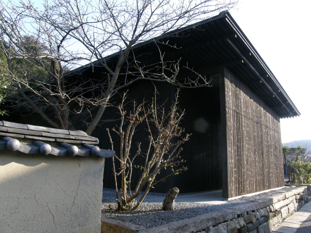 Exterior view of Minamidera, an Art House Project in Naoshima designed by Tadao Ando, featuring a minimalist wooden structure with dark charred cedar walls under a traditional gabled roof.