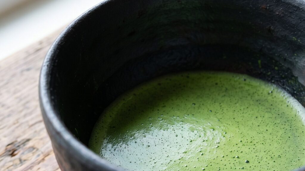 Black raku tea bowl with bright green matcha tea inside showing contrast between dark vessel and vivid green tea