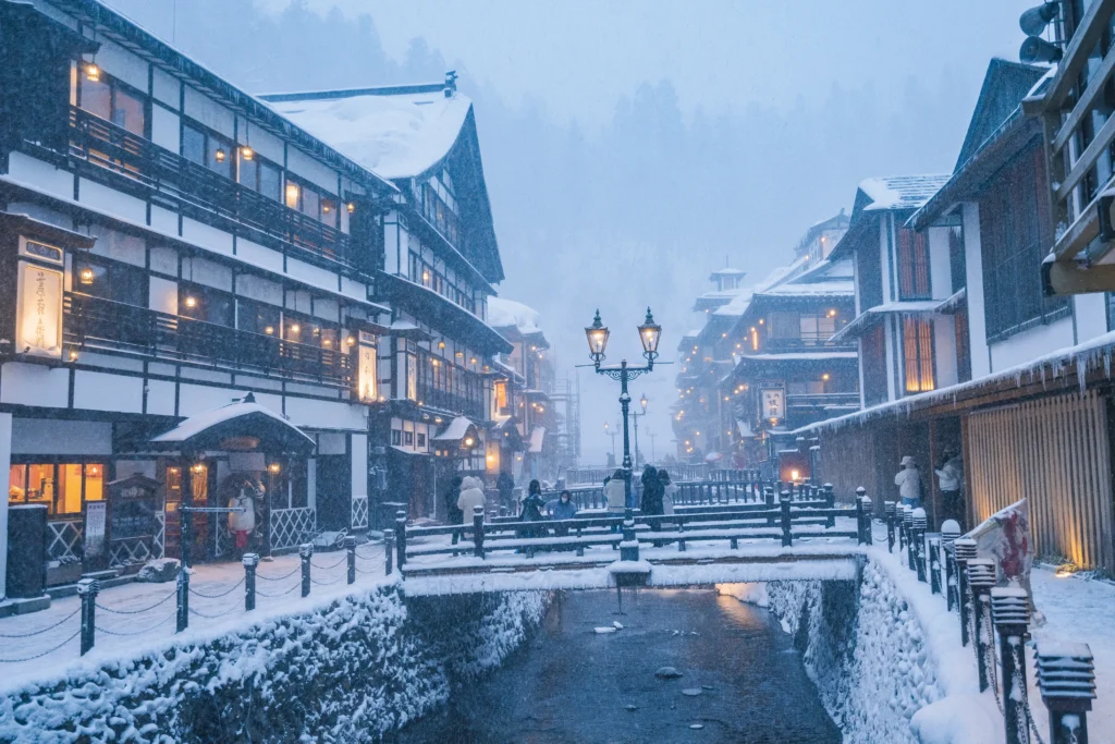 Ginzan Onsen Japan in winter snow covered wooden ryokan buildings warm light steam rising from river at night