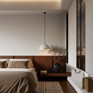A minimalist wabi-sabi style bedroom featuring a low bed with earthy brown linens. The room includes a dark wood paneled headboard that extends into a side shelf holding a black vase with budding branches. An organic-shaped white pendant light hangs from the ceiling, casting a warm glow. To the right, a sleek white wardrobe with glass panels and a woven basket are visible against clean white walls.