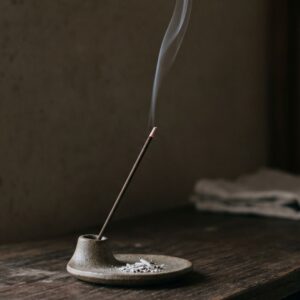 Japanese incense stick burning in ceramic holder with thin smoke trail rising in quiet room soft natural light
