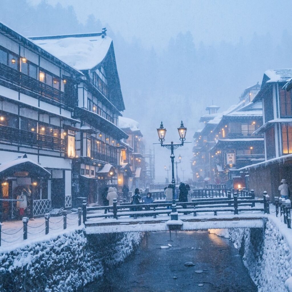 Ginzan Onsen Japan in winter snow covered wooden ryokan buildings warm light steam rising from river at night