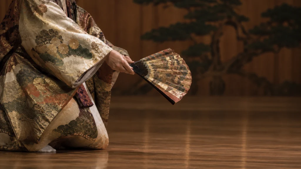 Noh theater performer hand holding folding fan precise gesture conveying Zeami teaching of controlled movement and hidden flower