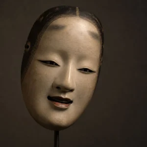 A traditional Japanese Noh mask displayed alone, slightly tilted, with an expression poised between joy and sorrow.